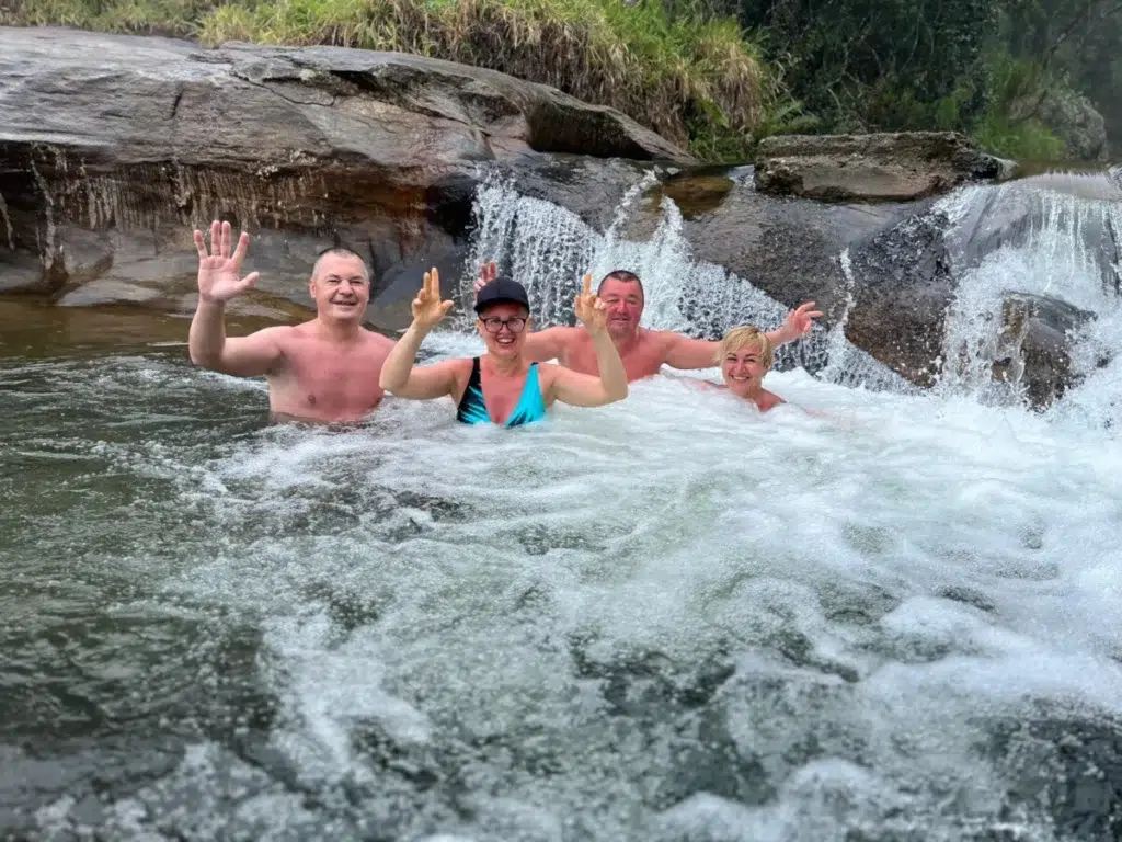 Travellers waving from a rocky pool at the foot of a river cascade