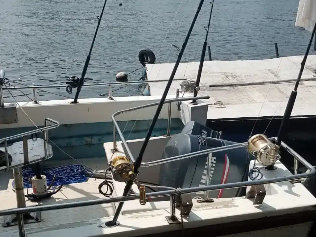 Fishing rods with large reels fixed along the rail of a small boat with an outboard motor, moored beside a concrete quay