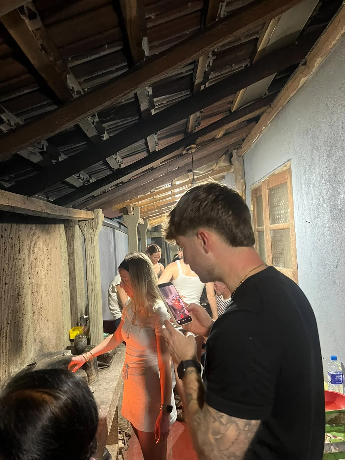 Guests gathered in a traditional Sri Lankan kitchen with wooden rafters during a village cooking class