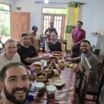 Cooking class guests and the host family seated around a table of Sri Lankan curries in clay pots
