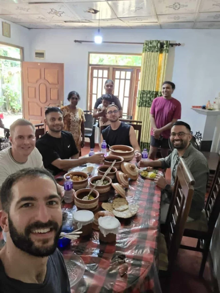 Cooking class guests and the host family seated around a table of Sri Lankan curries in clay pots