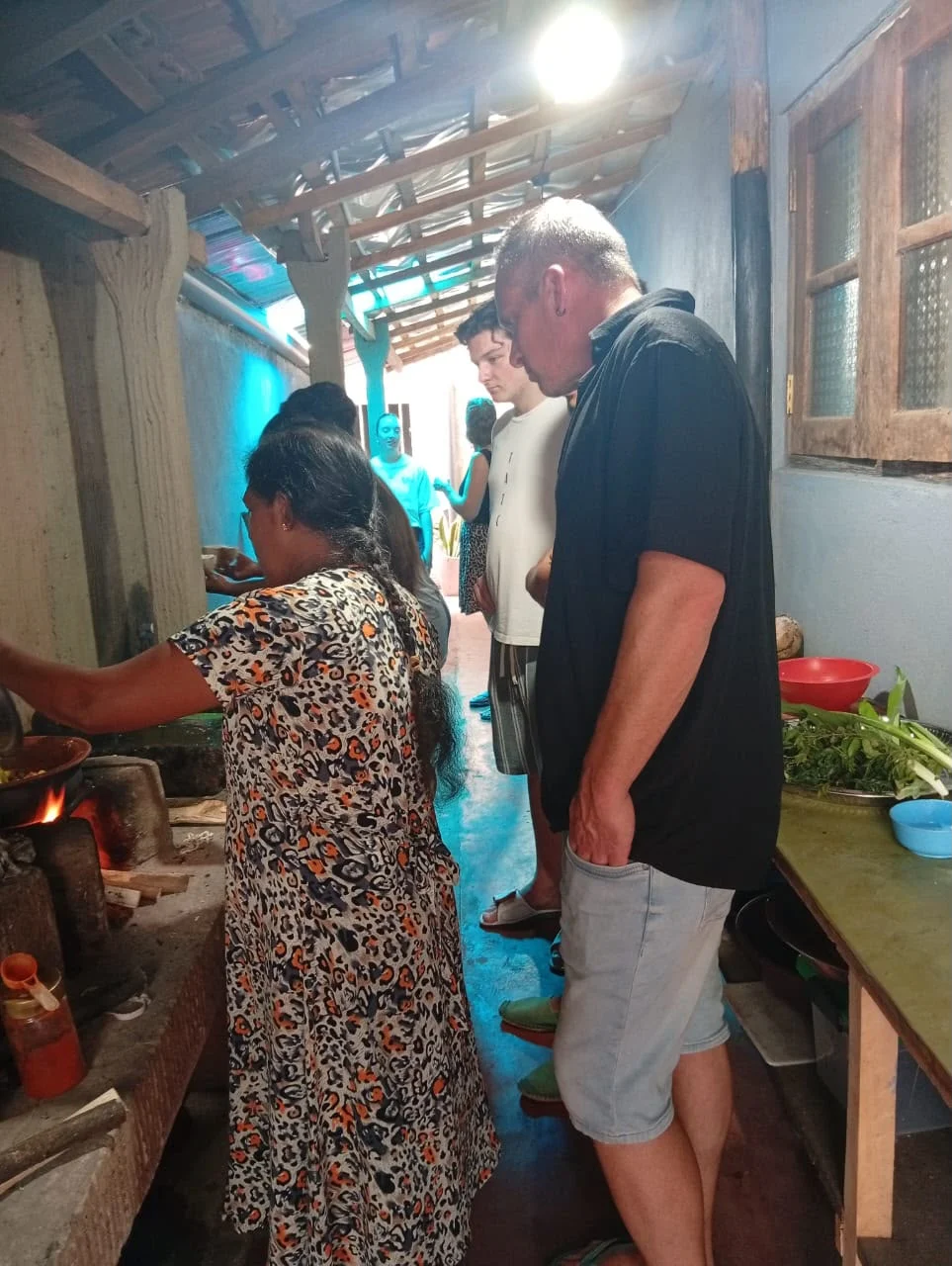 Sri Lankan host cooking over an open wood fire while cooking class guests watch