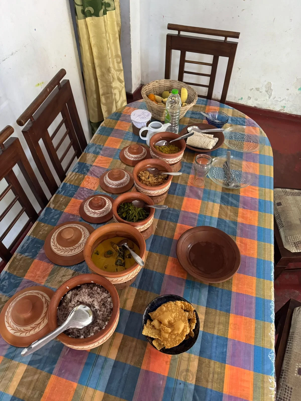 Sri Lankan rice and curry spread in clay pots on a village dining table, with red rice, dhal, green bean curry and papadam